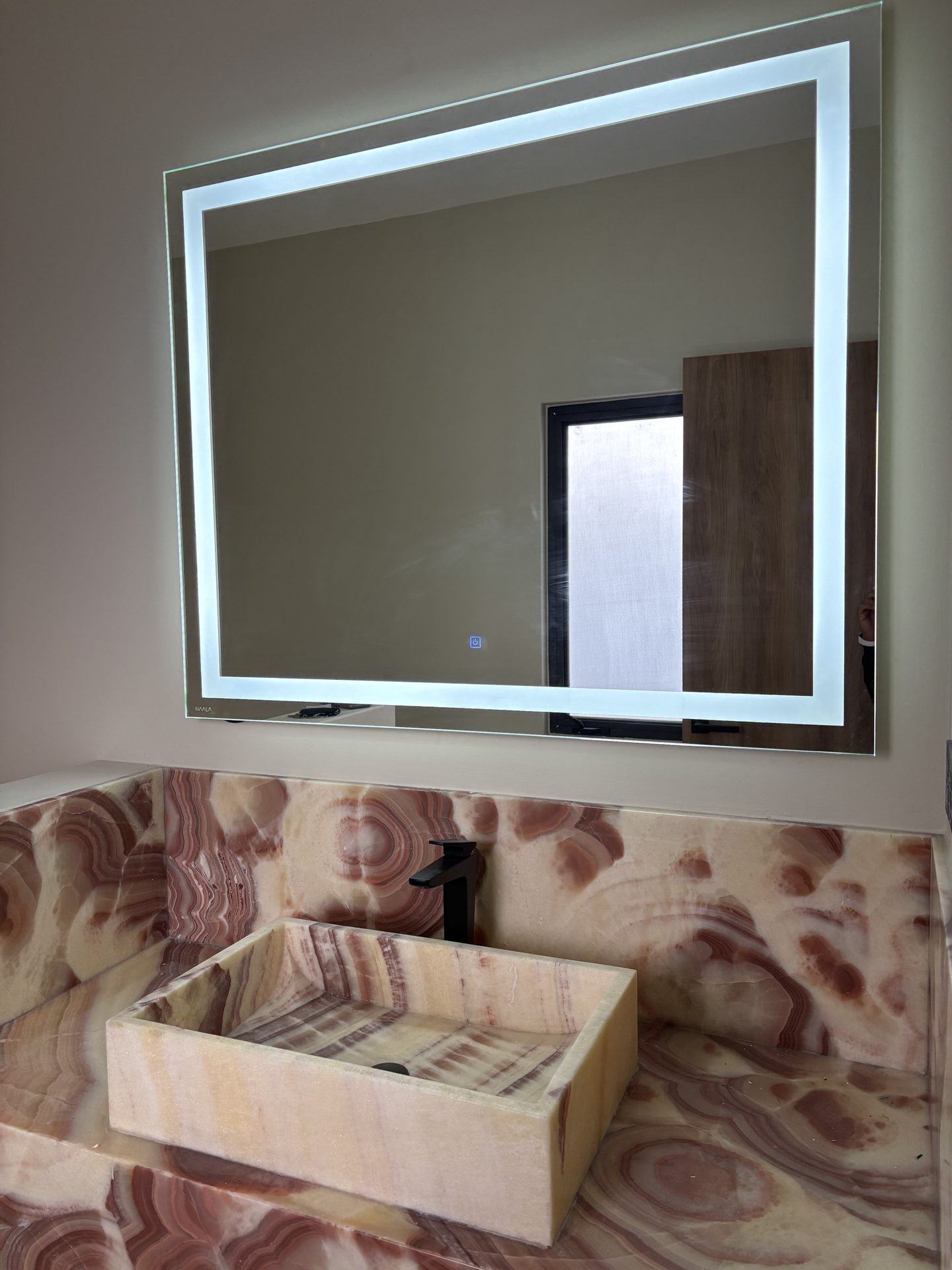 Espejo LED NAALA sobre lavabo de ónix en baño de Querétaro