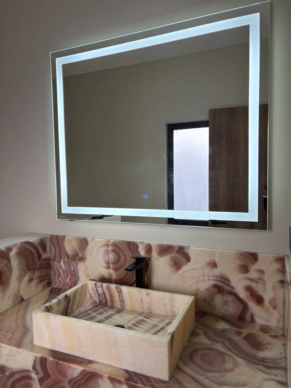 Espejo LED NAALA sobre lavabo de ónix en un baño residencial
